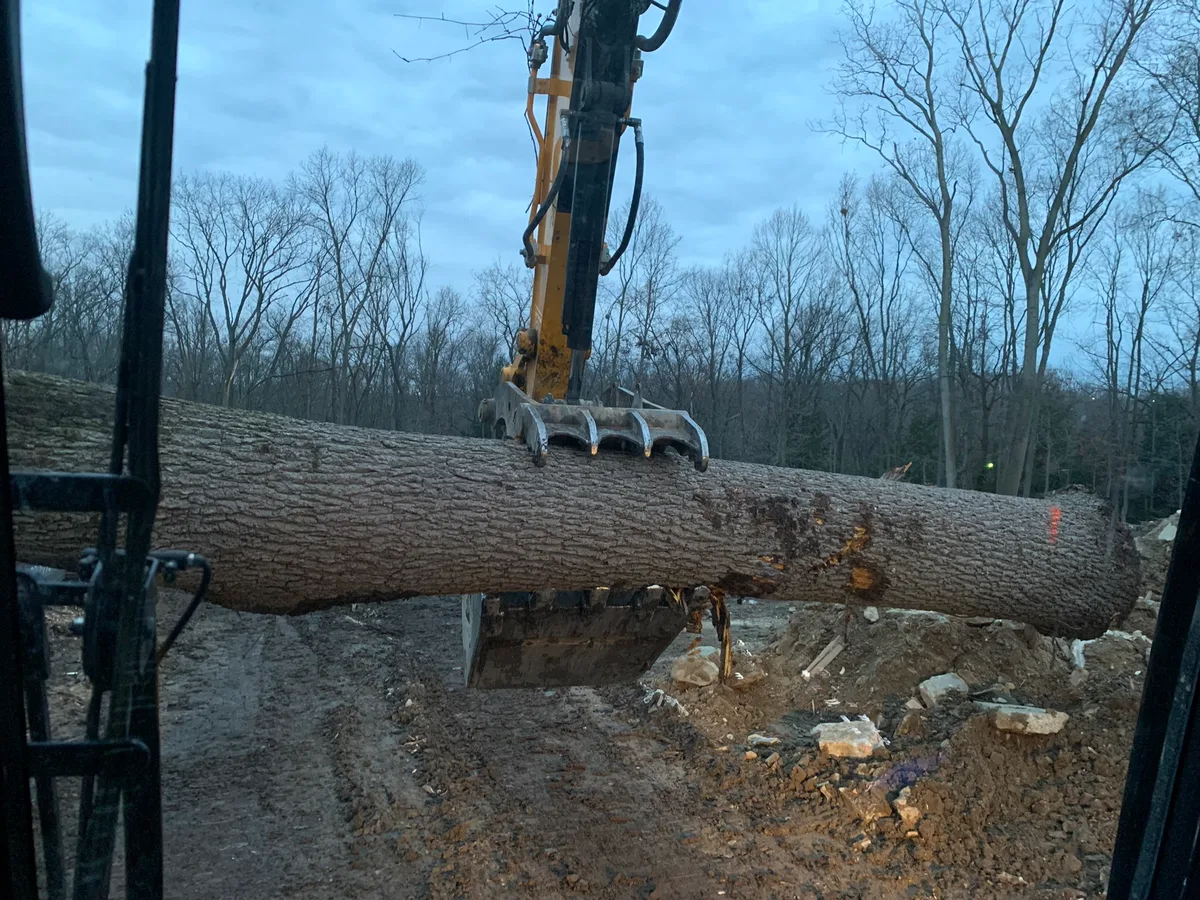 Excavator grapple lifting a large log on a cleared lot